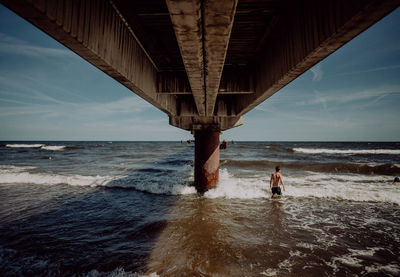 People on beach by bridge against sky