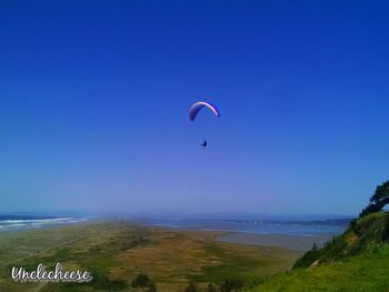 Low angle view of people paragliding against blue sky