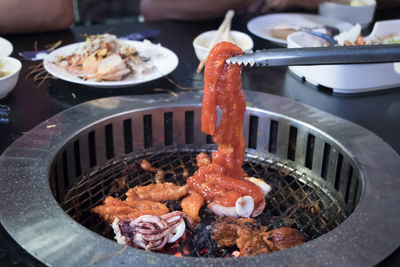 Roasted meat held by tongs above barbecue grill