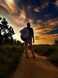 Rear view of man standing on field against sky during sunset