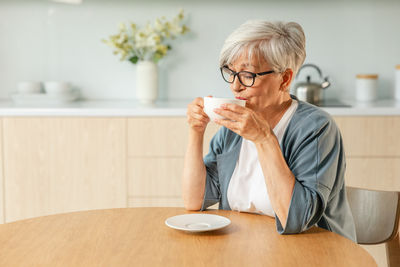 Young woman drinking coffee while sitting on table at home