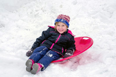 A cute little girl sits on her red saucer sled in the snow. what a fun way to enjoy winter
