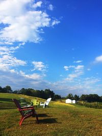 Empty bench on field against cloudy sky