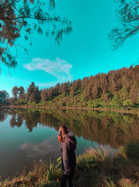 Rear view of young woman standing by lake against sky