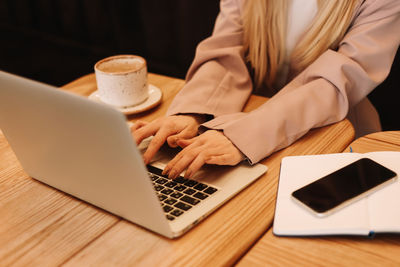 Human hands are typing on a laptop standing on a wooden table. desktop with a coffee mug