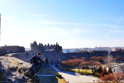 Young man gesturing peace sign while sitting on stone wall