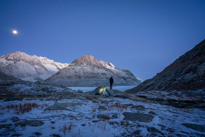 Person standing at lakeshore against snowcapped mountains