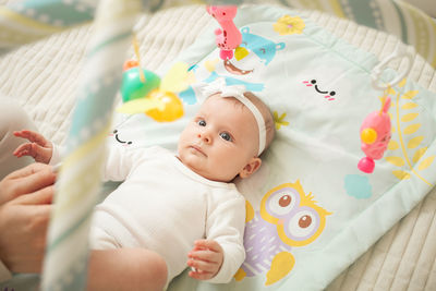 Child lies on bed, hanging toys, baby mat, newborn girl. developing, watching toys, satisfied. 