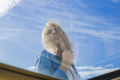 Low angle view of mid adult woman standing against blue sky seen through car window