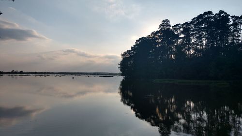 Silhouette trees by lake against sky during sunset