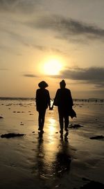 Silhouette people on beach against sky during sunset