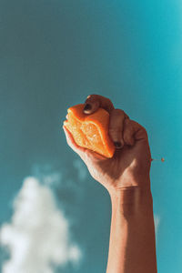 Cropped hand holding orange shape against blue sky