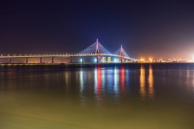 Illuminated bridge over river against sky at night