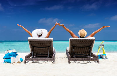 Rear view of couple relaxing on lounge chairs at beach