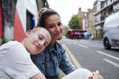 Non-binary person leaning head on woman's shoulder at street