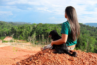 Woman sitting on street amidst trees against sky