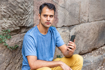 Young latin man with mobile phone sitting outside