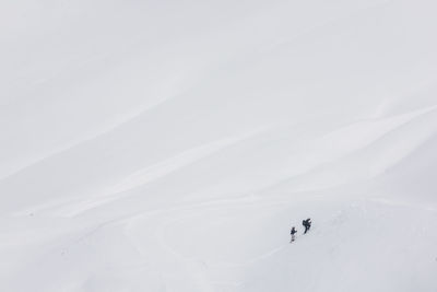 Minimalistic cold winter landscape with white snowy mountain ridge slope and climbing mountaineers