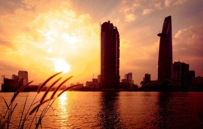 Scenic view of river by buildings against sky during sunset