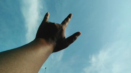 Low angle view of hand gesturing against sky
