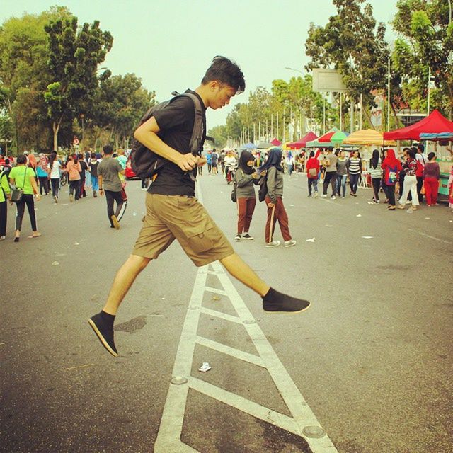 tree, men, large group of people, lifestyles, transportation, street, leisure activity, person, road, sport, day, outdoors, mid-air, sunlight, walking, incidental people, road marking, flying, motion