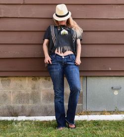 Young woman covering face with hat while leaning on wall