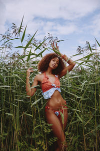 Young woman in bikini standing on field against sky