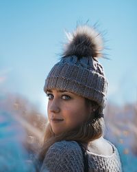 Portrait of young woman wearing knit hat while standing against blue sky