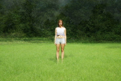 Portrait of young woman standing on grassy field against trees