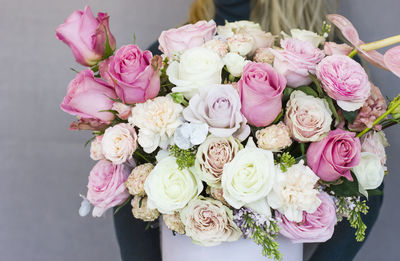 The beautiful bouquet of different roses in white box in female hands on gray background