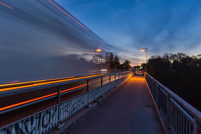 Light trails on bridge over street against sky