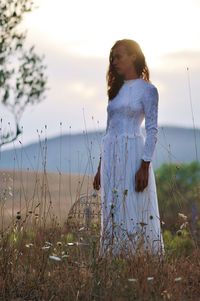 Bride holding birdcage while standing against sky