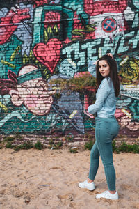 Portrait of young woman standing against graffiti wall at beach
