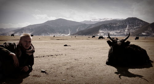 Portrait of man with animal sitting on sand against mountains