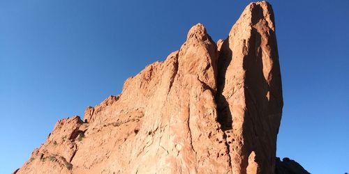 Low angle view of rocky mountain against clear blue sky