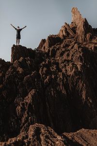 Low angle view of person standing on rock against sky