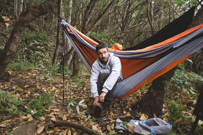 A man sitting in a hammock in the forest gets prepared for hiking person
