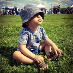 Boy wearing bucket hat while sitting on grassy field