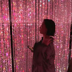 Side view of woman standing against illuminated light at night