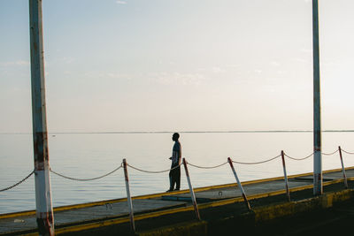 Rear view of man walking on pier against sky