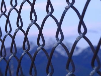 Close-up of chainlink fence against sky during sunset