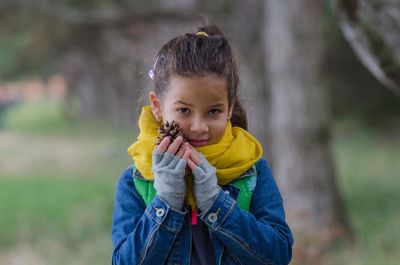 Portrait of girl holding pine cone while standing against trees