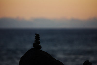 Close-up of silhouette rock on shore against sky during sunset