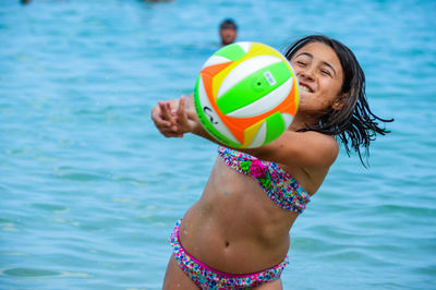 Smiling young woman with ball while standing at beach