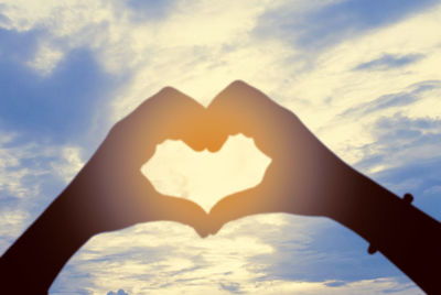 Close-up of woman hand heart shape against sky