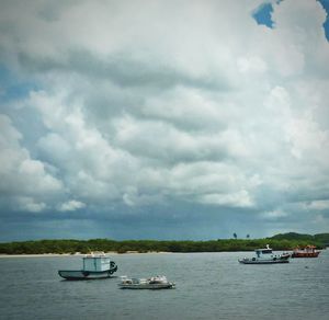 Boats sailing in sea against cloudy sky