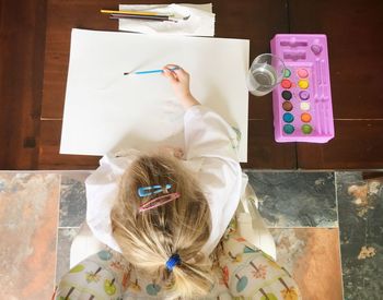 Directly above shot of girl painting on paper at wooden table