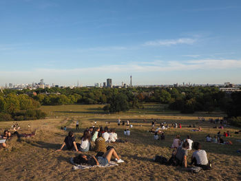 Group of people relaxing on field against sky