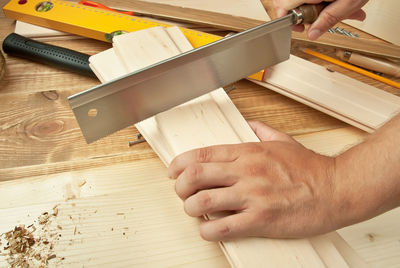 Close-up of craftsperson cutting wooden plank with hand saw