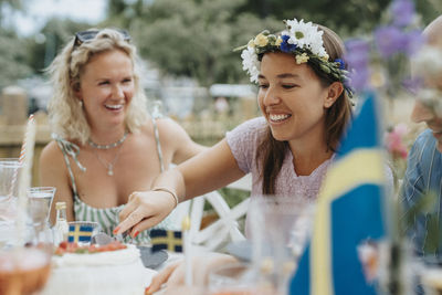 Smiling woman cutting cake with friends during dinner party at cafe